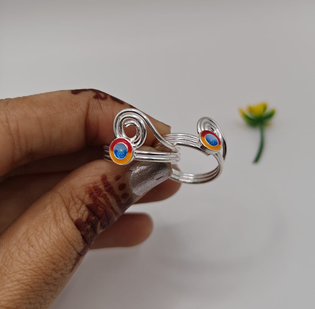 silver toe ring featuring two circular colorful inlays with red, orange, and blue details