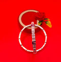 A silver-toned bangle bracelet with engraved motifs and a central hanging charm, displayed against a bright red background with a blurred decorative box and flower.
