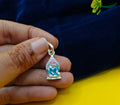 A hand holding a small silver pendant featuring a seated figureof Sai