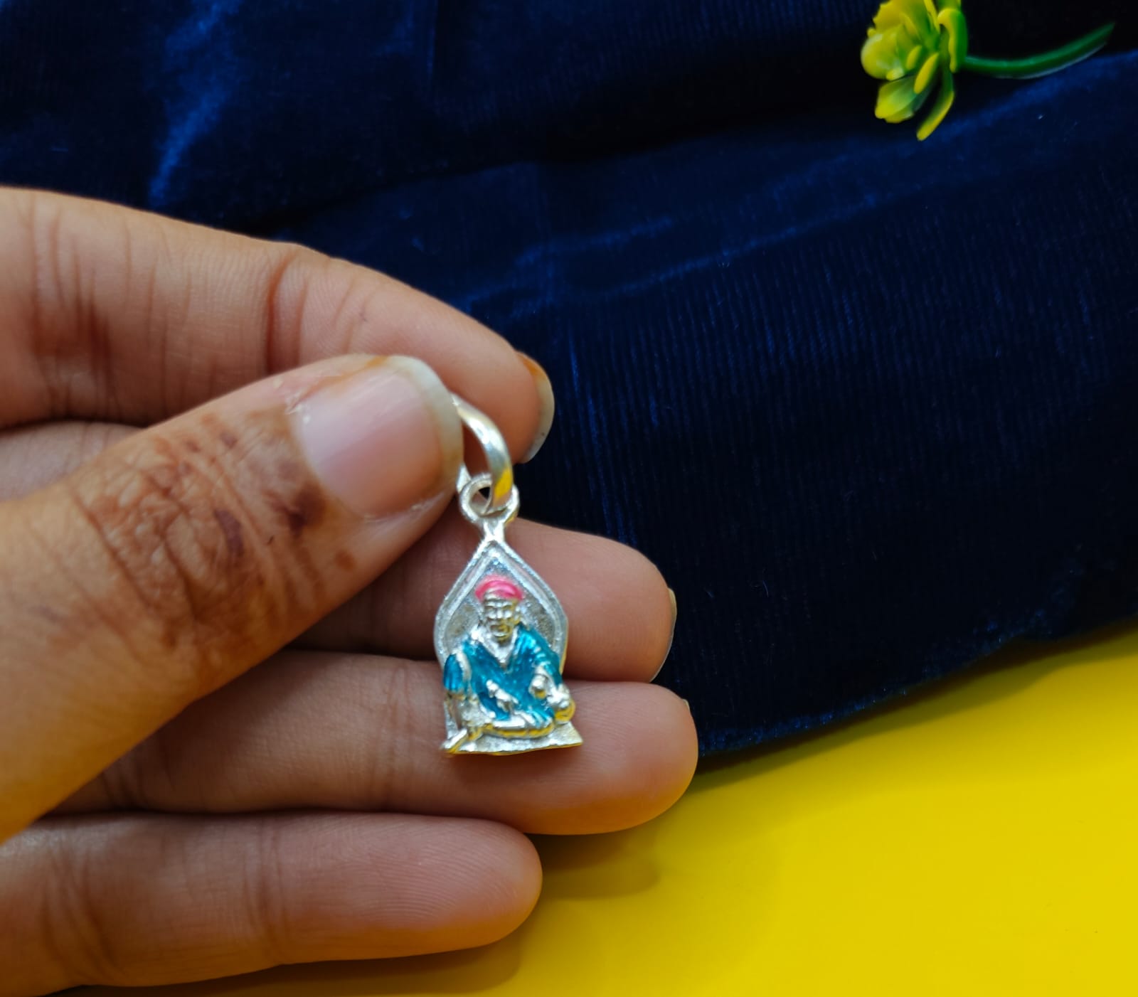 A hand holding a small silver pendant featuring a seated figureof Sai