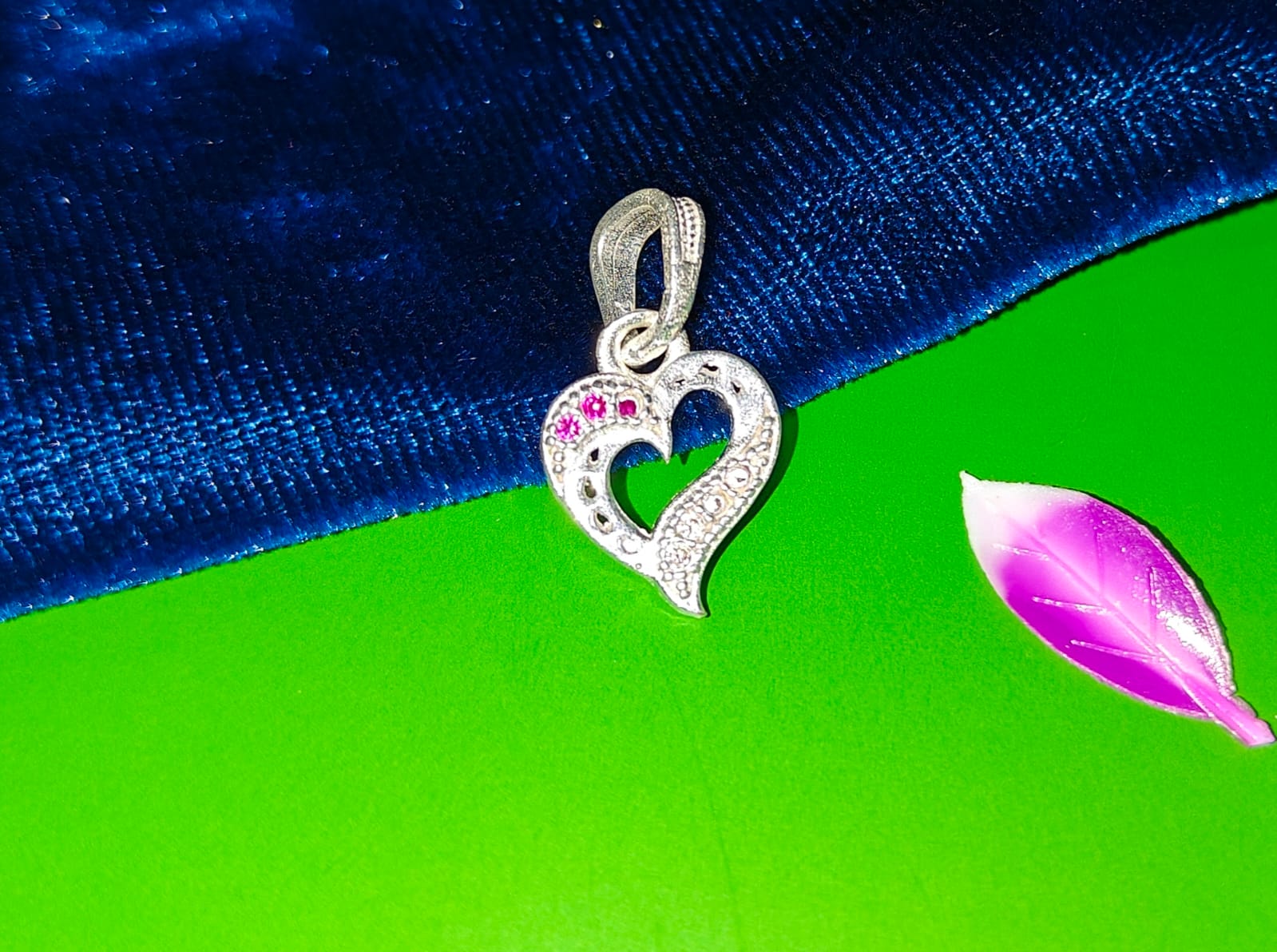 A silver heart-shaped pendant with a pavé-set clear crystal border and a small row of pink gemstones.