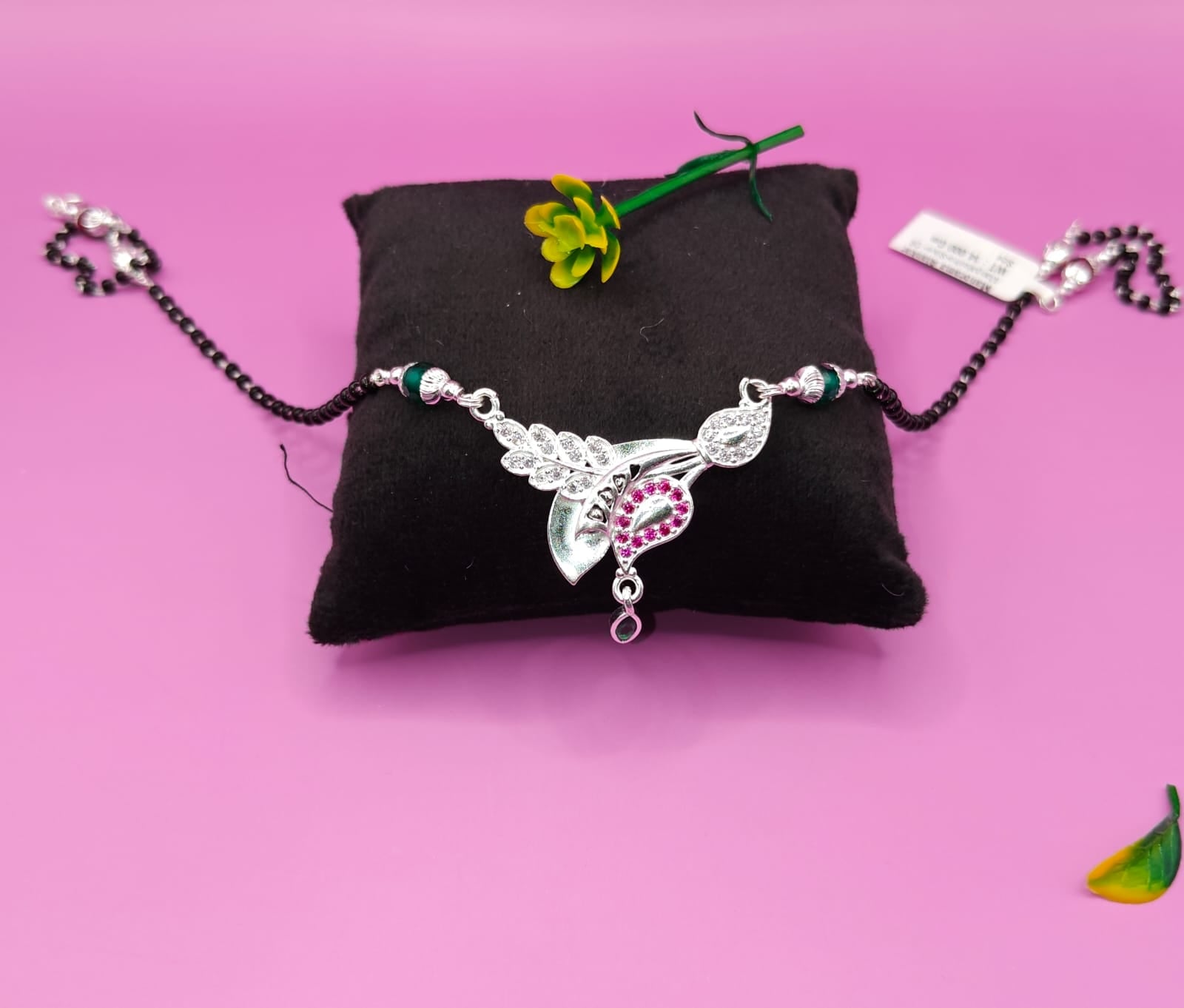 A silver-toned mangalsutra with a decorative pendant featuring a silver leaf and a pink heart-shaped stone