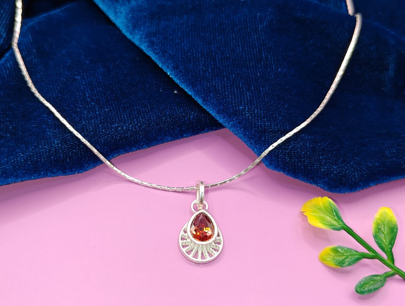 A silver teardrop pendant necklace with a faceted orange-red gemstone.