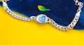 A silver-toned curb chain bracelet with a central oval charm featuring a cartoon character, displayed on a split yellow and dark blue background.