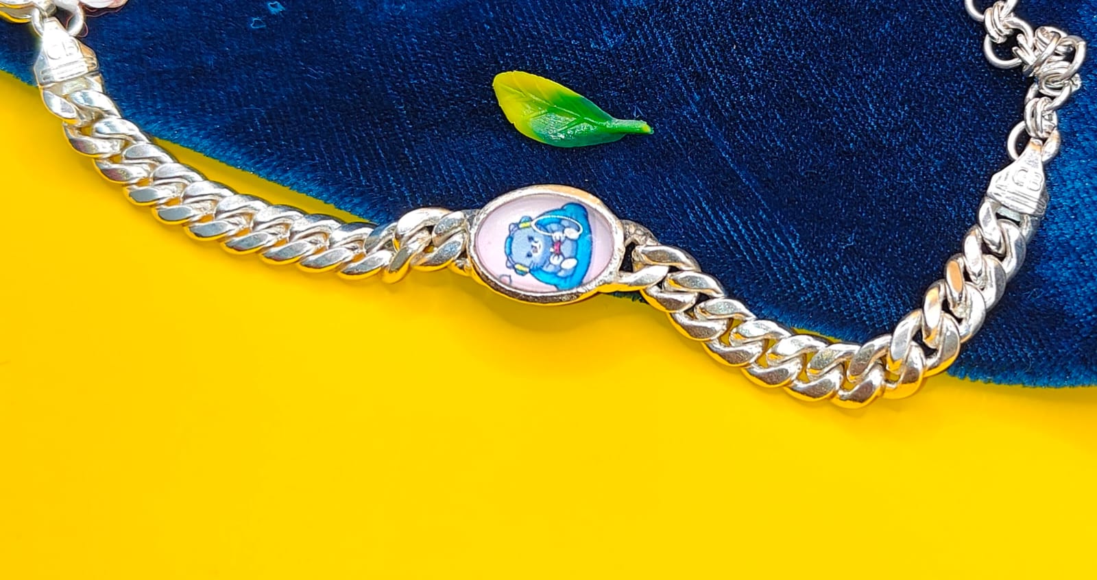 A silver-toned curb chain bracelet with a central oval charm featuring a cartoon character, displayed on a split yellow and dark blue background.